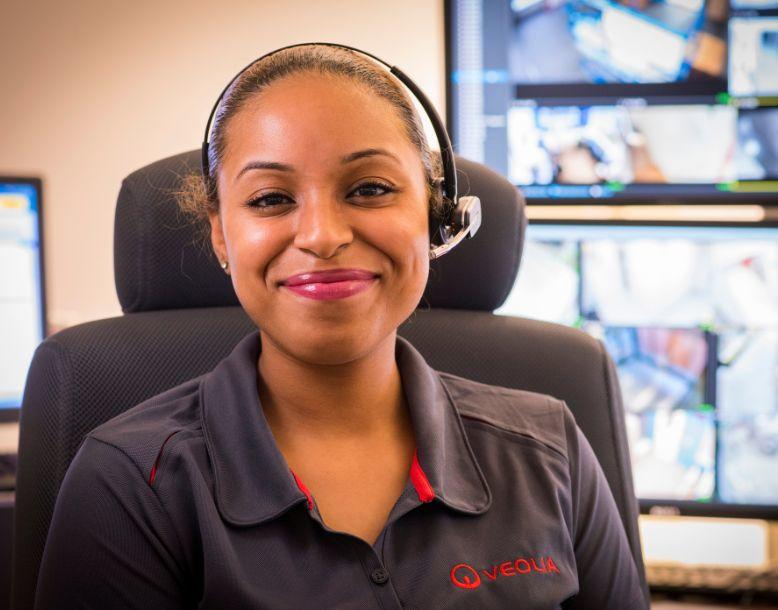 A Veolia employee sitting in an office smiles at the camera wearing an audio headset